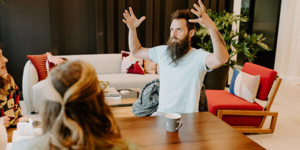 Benj sitting at a meeting table with his hands in the air and coffee on the table, talking to someone about b2b marketing