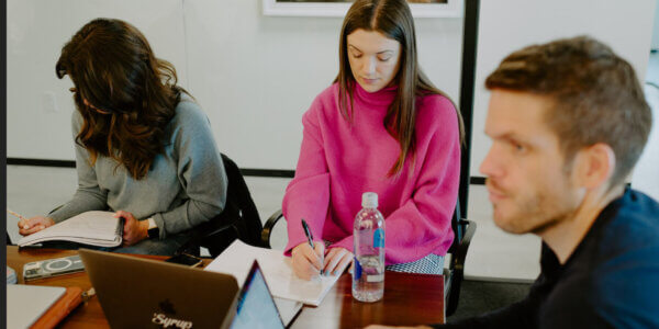 Group of 3 Syrup team members sitting at an office table taking notes during a meeting about employee and client retention