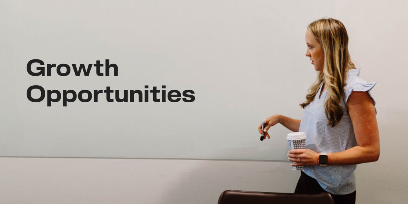 Kate looking at whiteboard that says Growth Opportunities while holding marker and coffee cup