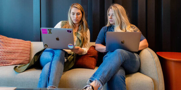 Two Syrup team members sitting on a couch with laptops discussing integrating sales and marketing