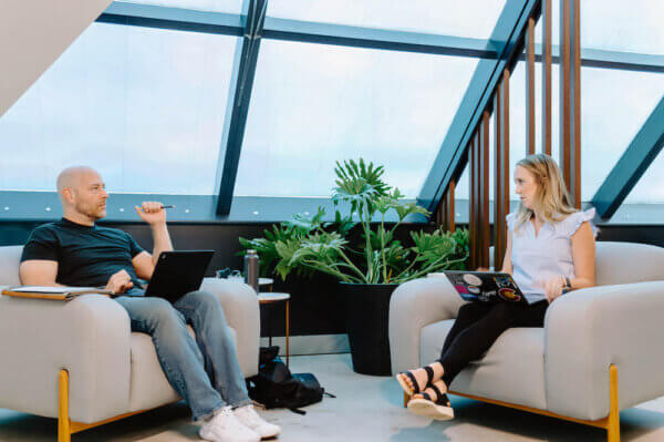 Jason and Kate sitting in chairs with laptops on their laps having a meeting