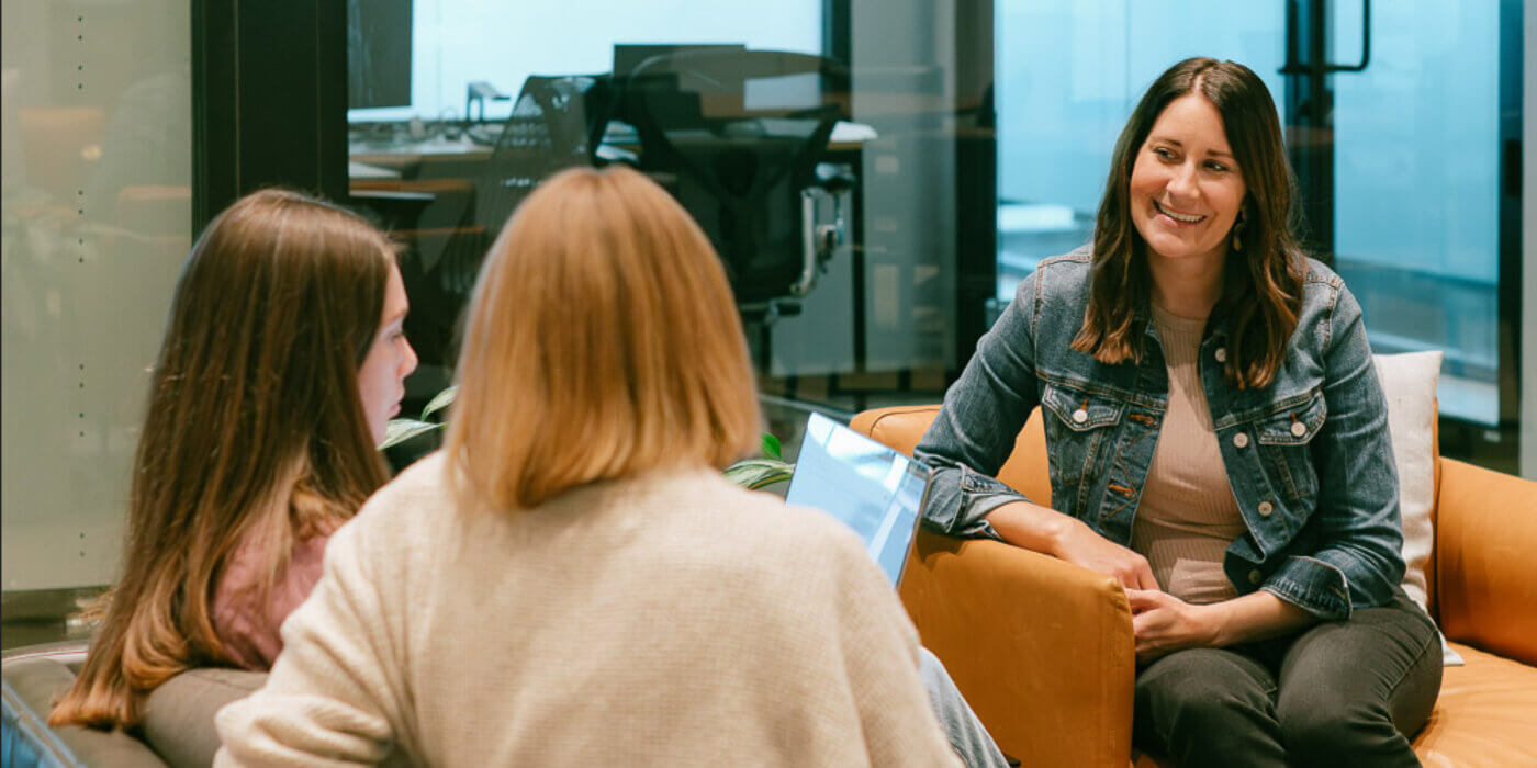 Girl sitting on couch looking at two other girls sitting on opposite couch talking through building trust in b2b