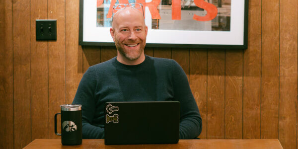 Jason sitting at the head of a table with a laptop open and coffee cup discussing Messaging for B2B Sales and Marketing Teams