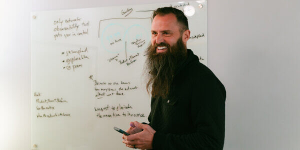 Man holding a phone smiling with whiteboard behind him