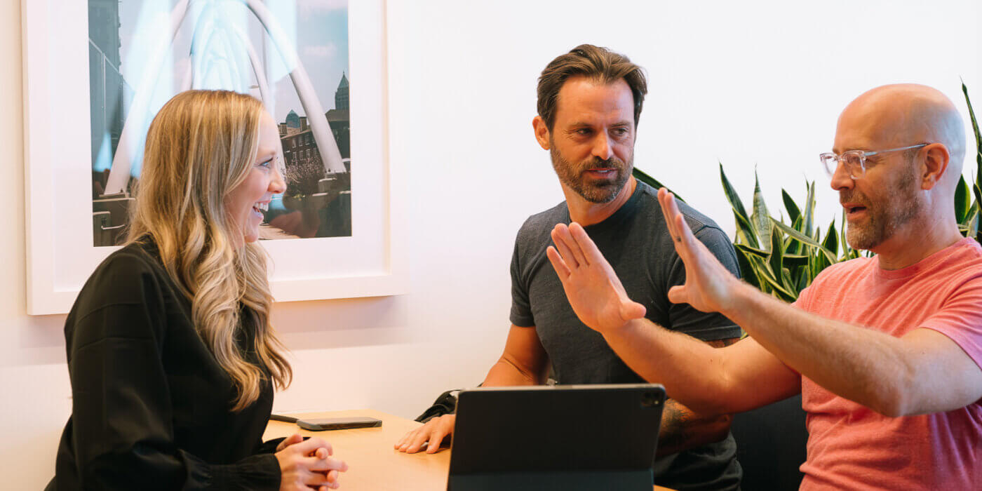 Three people sitting in a booth with a laptop discussing the certainty-uncertainty paradox