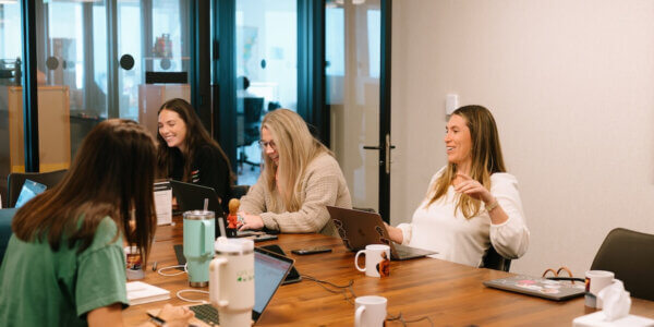 Group of Syrup employee advocates sitting around table with laptops open talking and smiling