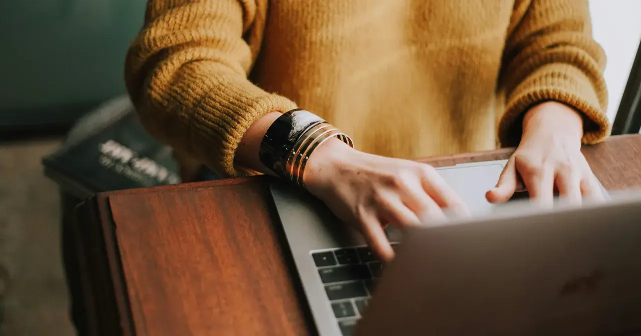 Woman in yellow sweater typing on computer