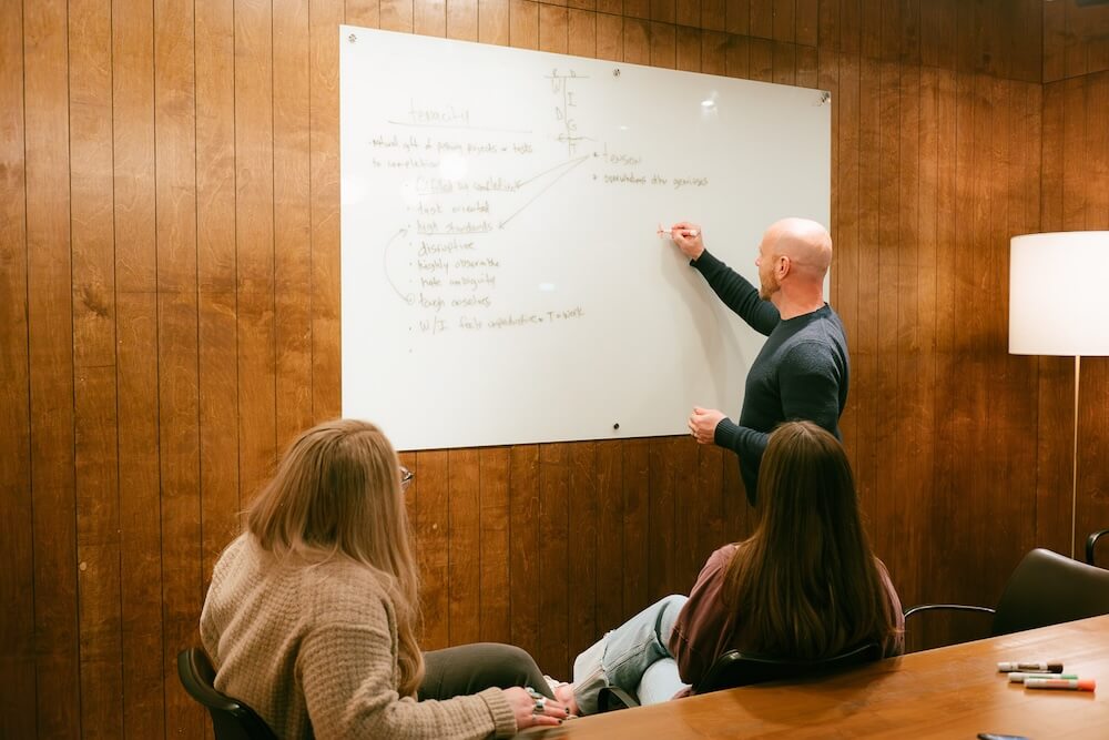 Jason drawing on a whiteboard on the wall with two women watching while he talks through 2026 plans