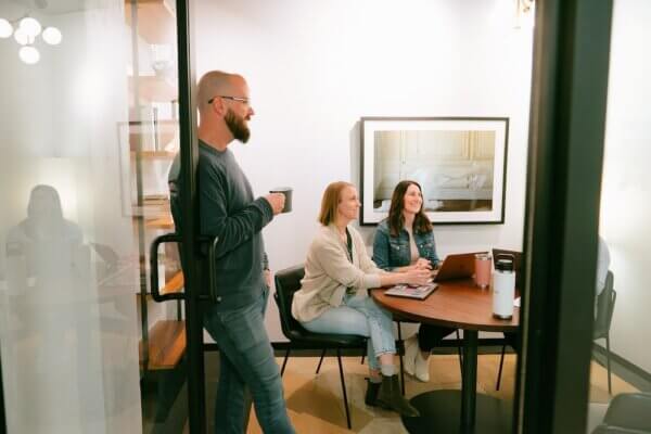 3 people standing and sitting around office room smiling while discussing aeo and seo