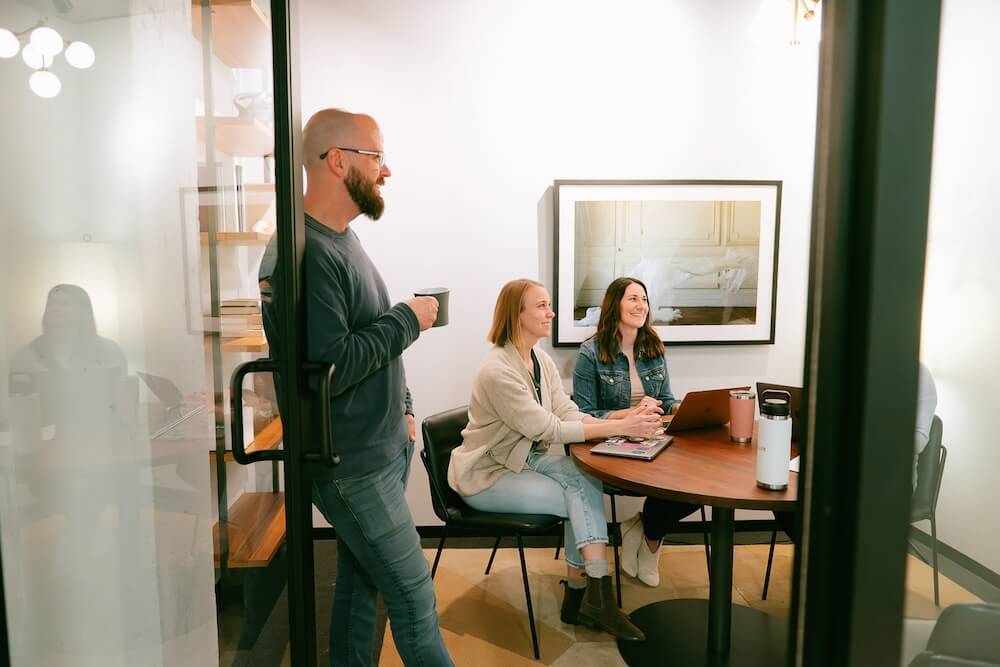 3 people standing and sitting around office room smiling while discussing aeo and seo