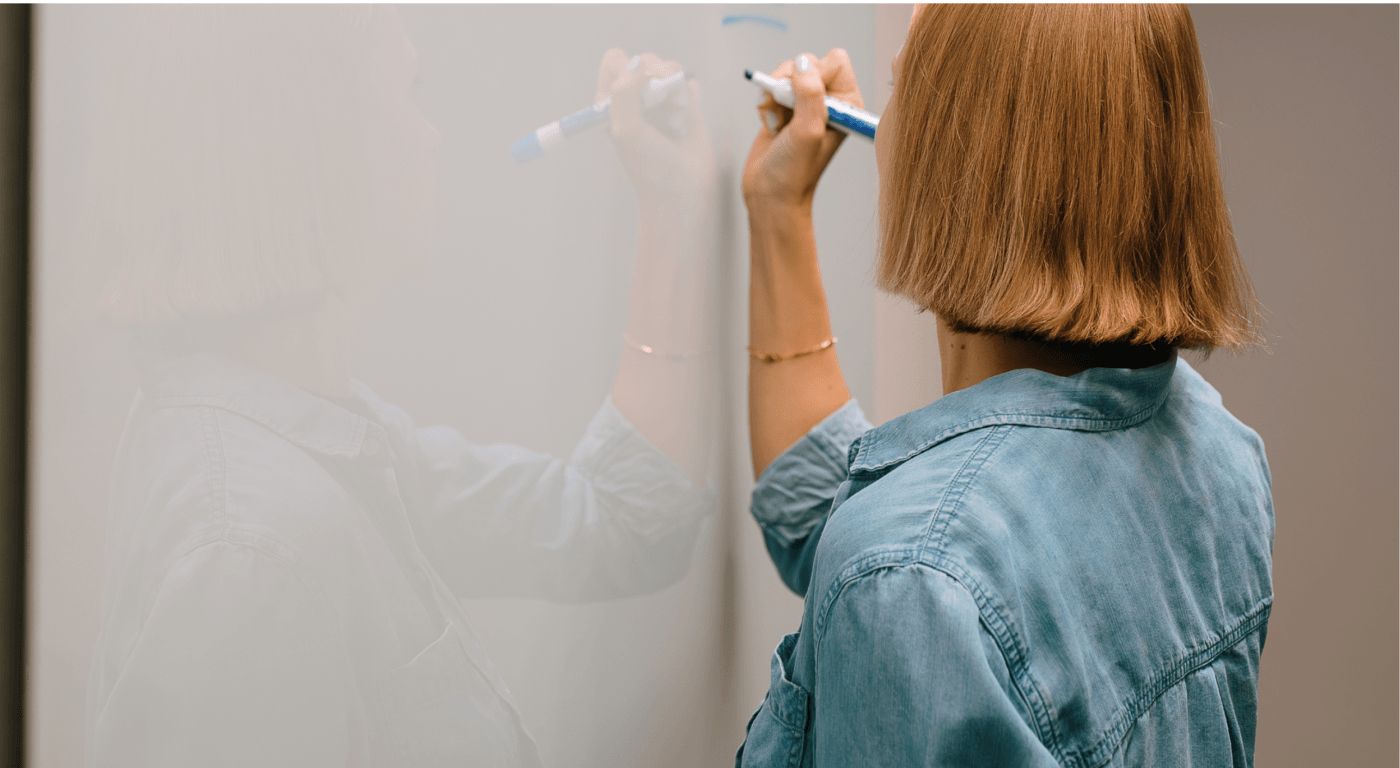 Woman facing whiteboard writing marketing checklist on it with marker