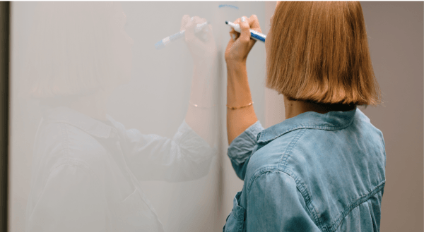 Woman facing whiteboard writing marketing checklist on it with marker