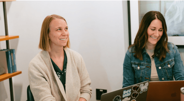 Two woman sitting at a table smiling and discussing ai content watermarks