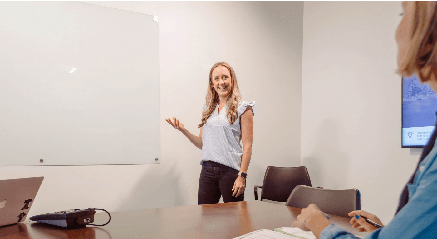 Kate standing in front of table of people, pointing at white board discussing B2B ideal client profile